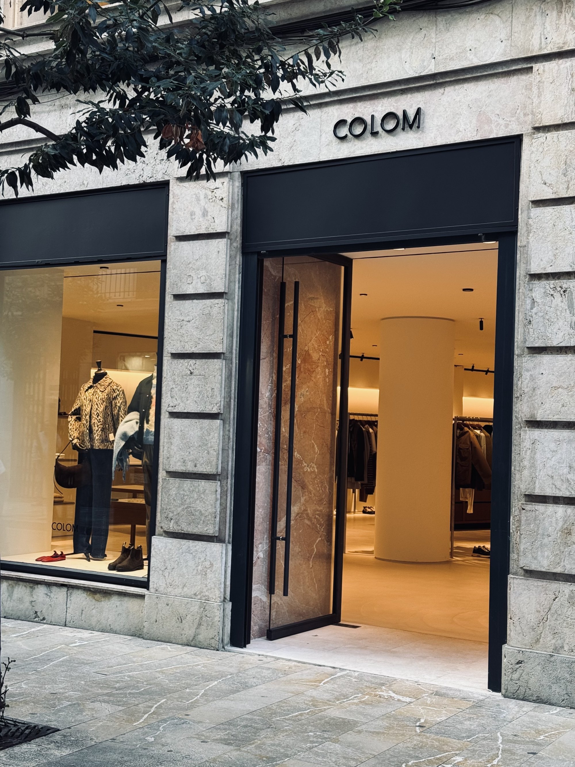 The stone-fronted entrance to Colom in Palma, with its black sign, open doorway and fashion display visible through the window.
