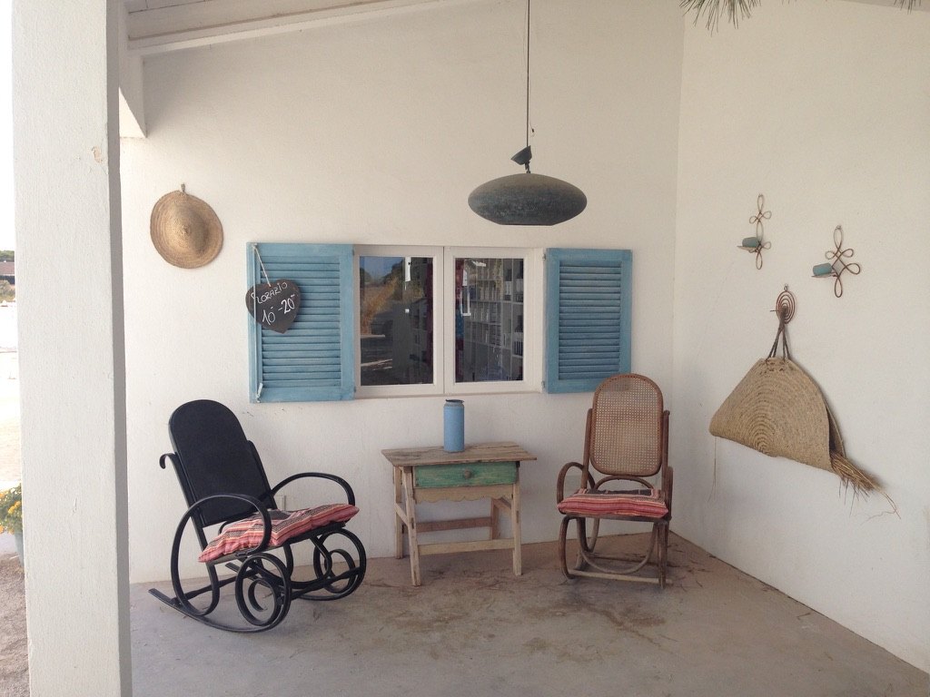 Two rocking chairs beside a small table and pale blue shutters in the ice-cream seating area next to the Flor de Sal shop.